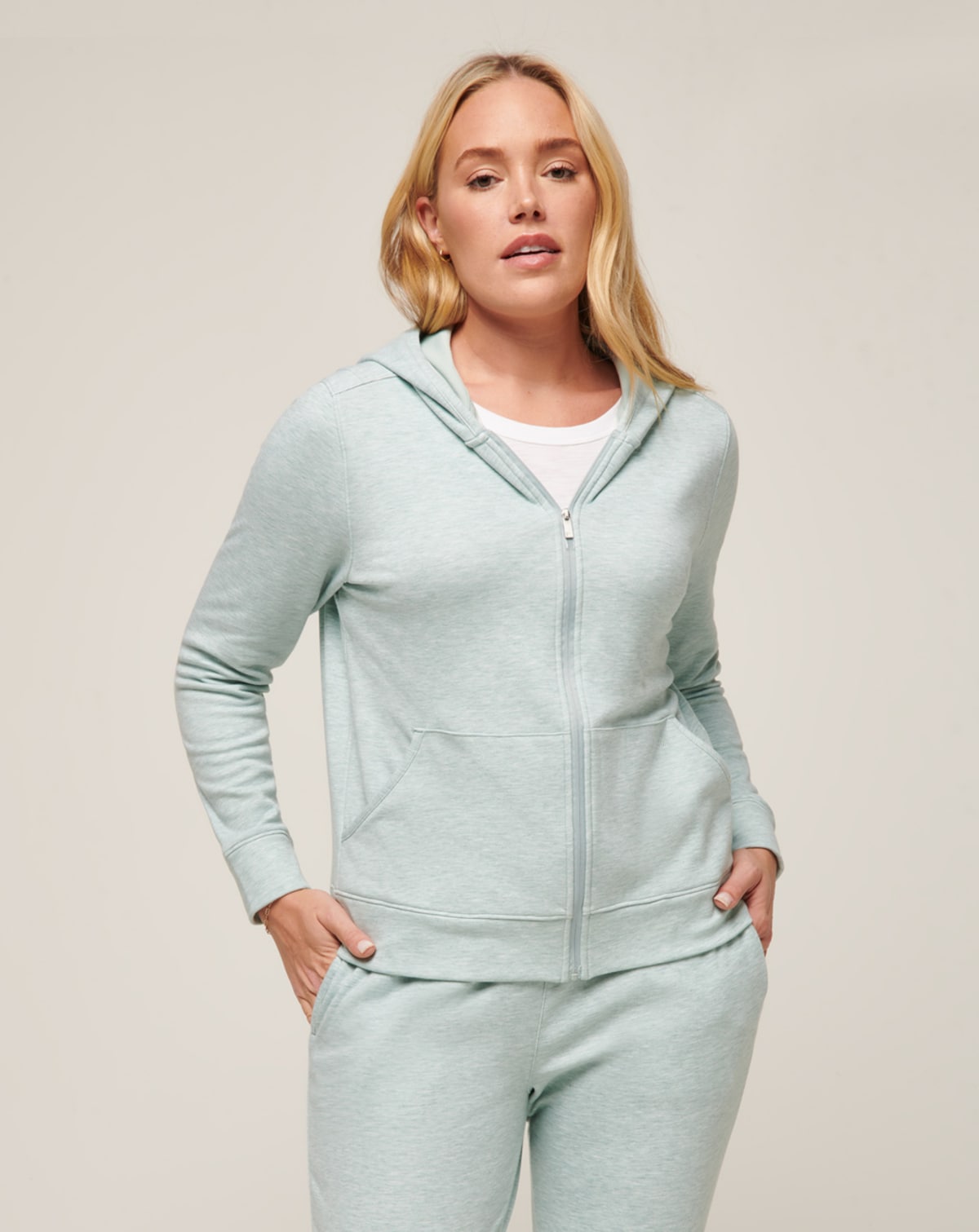 Light teal zip-up hoodie and matching sweatpants; woman modeling comfortable loungewear.