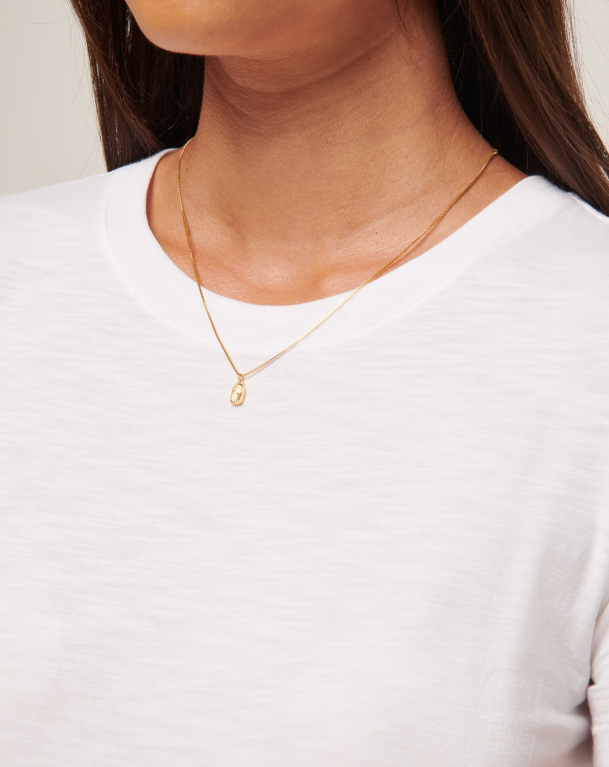 Gold necklace with small pendant on a white shirt.