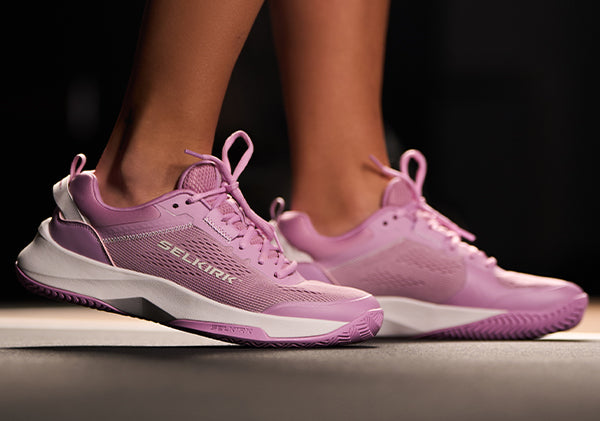 Lavender women's athletic shoes with white soles, shown on a dark background.