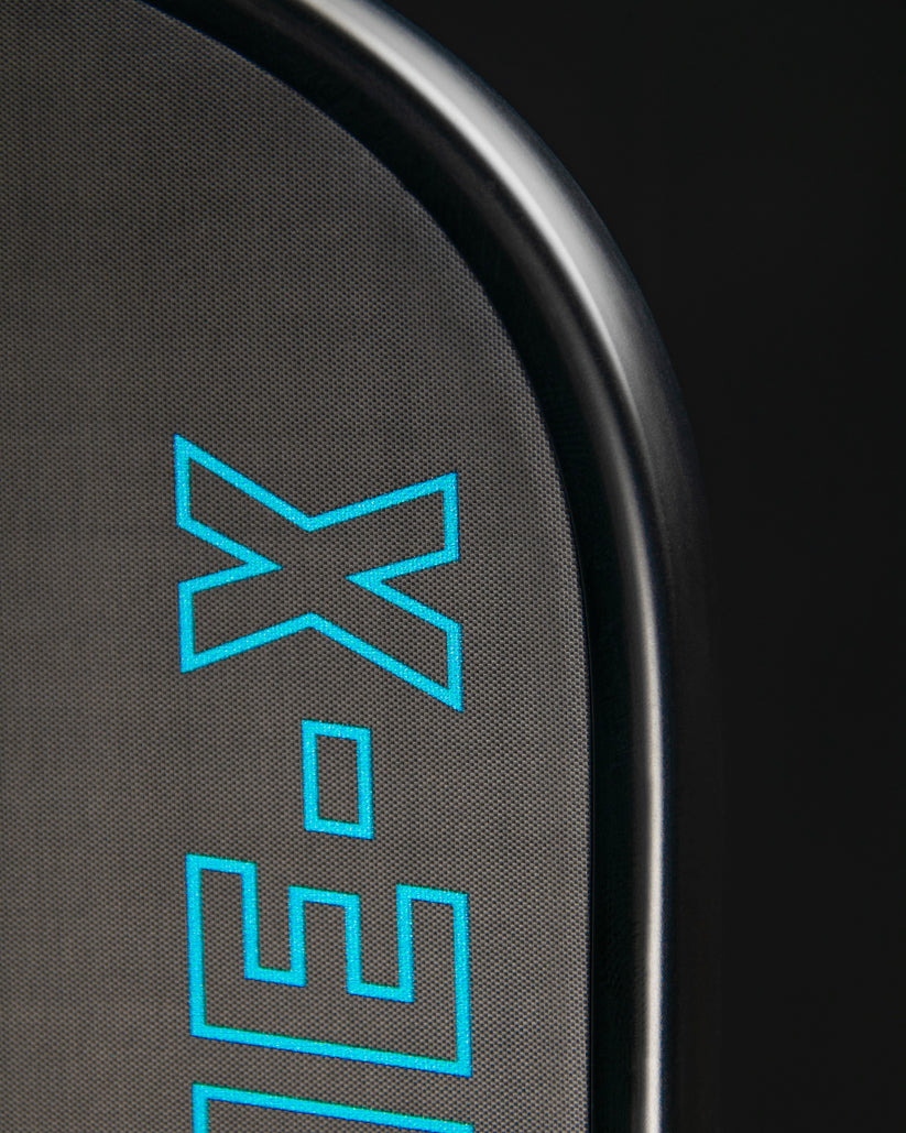 Close-up of textured black paddle face with teal logo detail.