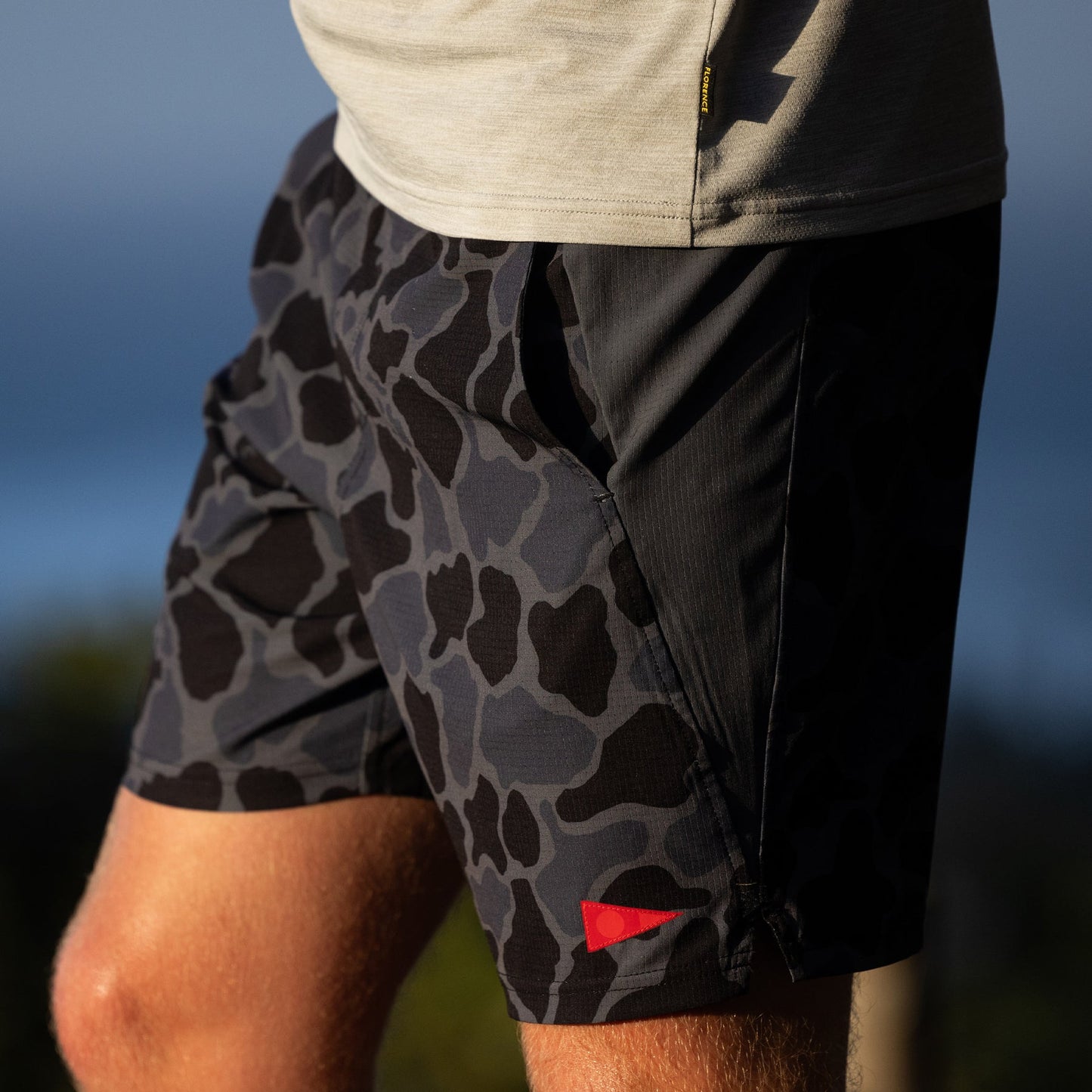 Gray and black camouflage print shorts with a side pocket, worn outdoors.