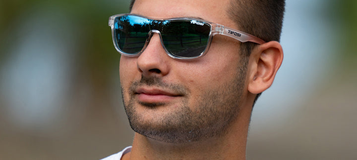 Man wearing clear-framed sunglasses with bright blue mirrored lenses outdoors.