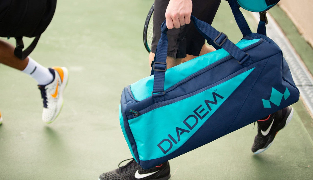 Teal and navy blue duffel bag carried on a tennis court.
