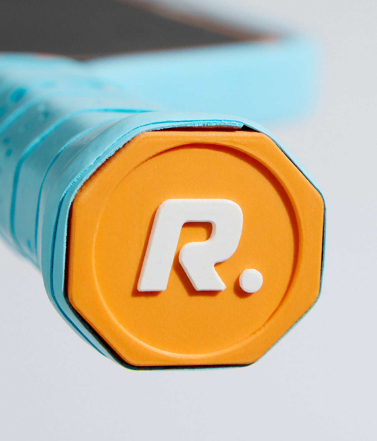 Close-up of a light-blue and orange pickleball paddle grip, featuring a logo.