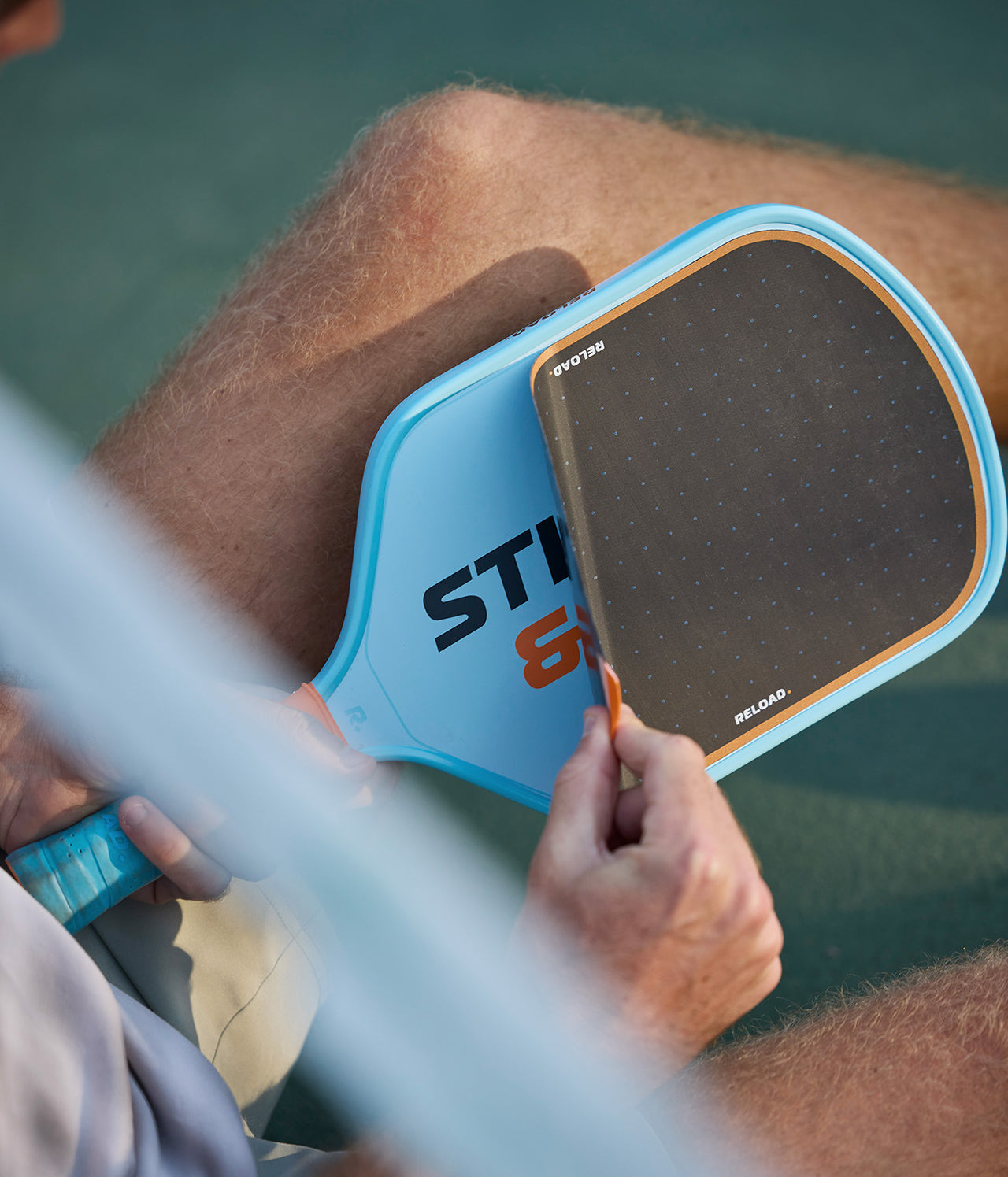 Person installing dark gray pickleball paddle grip, light blue paddle face.