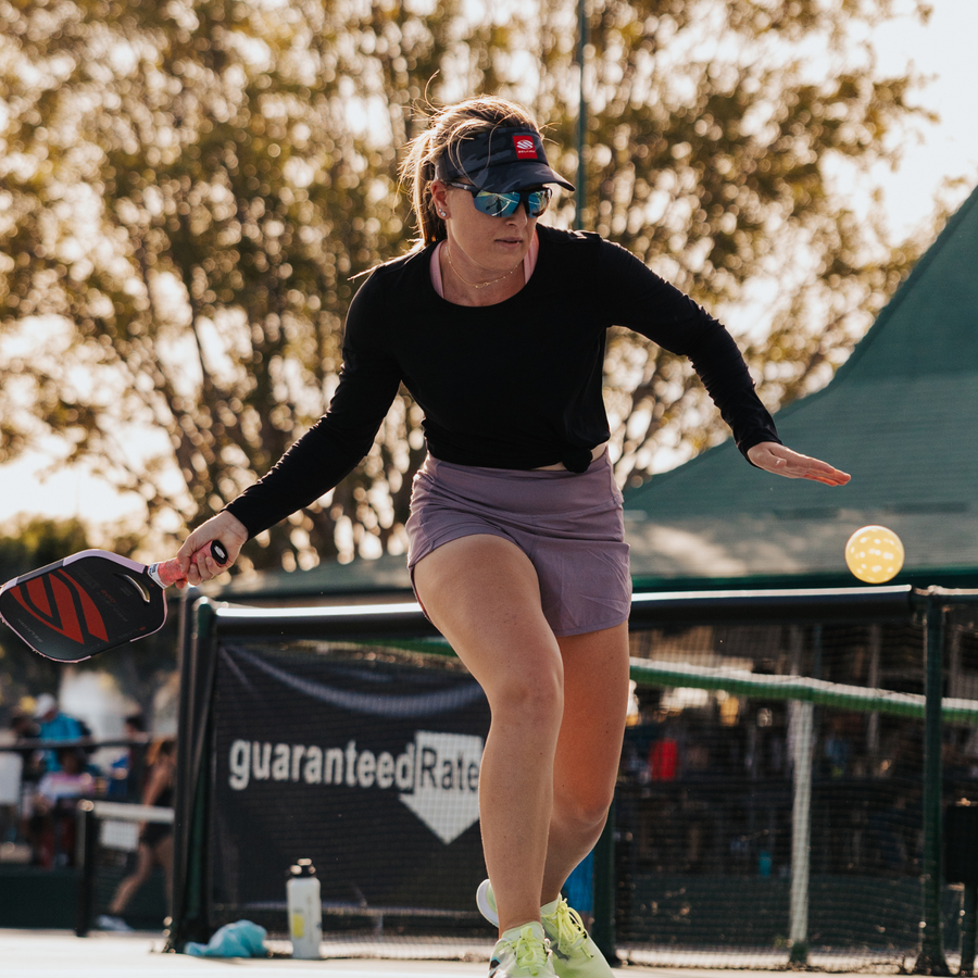 Woman playing pickleball, wearing sunglasses and a visor, during an outdoor match.