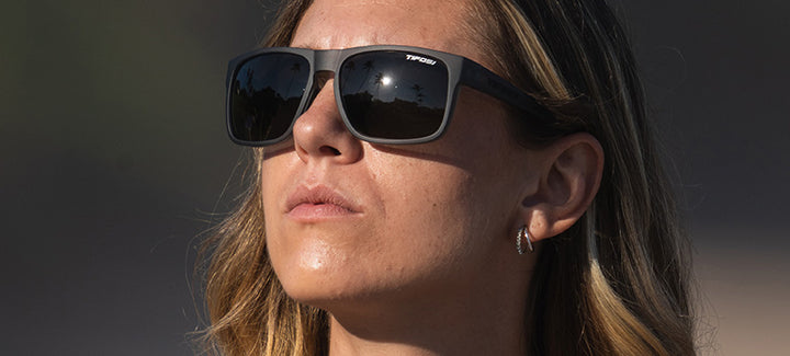 Woman wearing matte gray sunglasses outdoors, reflecting sunlight.