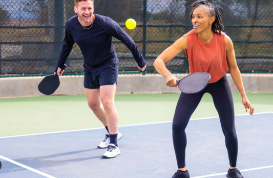 Two people playing pickleball on an outdoor court.
