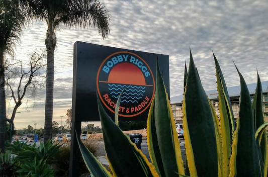 Outdoor sign with sunset graphic, partially obscured by agave plant.