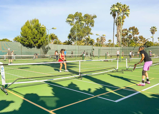 Outdoor pickleball game on sunny day, players on green court.