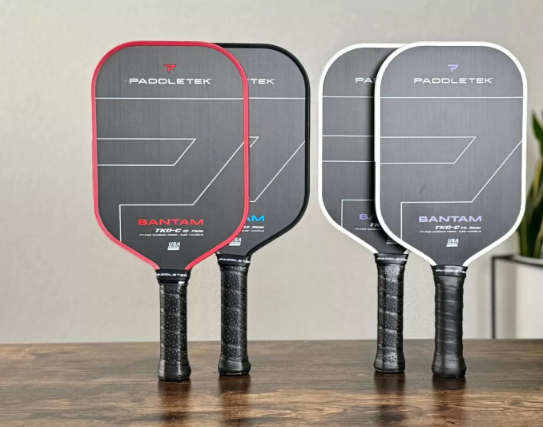 Three Bantam pickleball paddles with graphite faces and textured grips; red, black, and white edges.