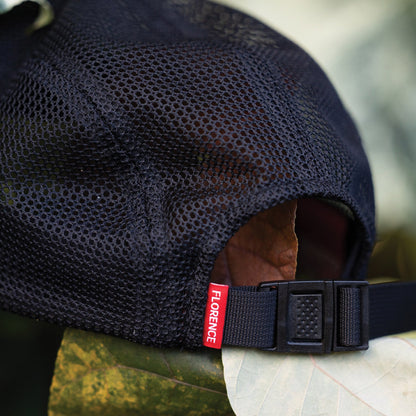 Black unstructured hat with breathable mesh back, adjustable strap, and red label detail.
