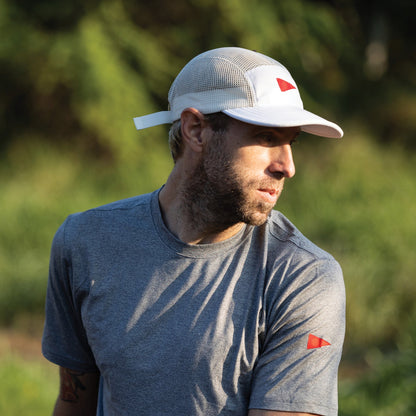 Man wearing a white unstructured mesh hat outdoors in sunlight.
