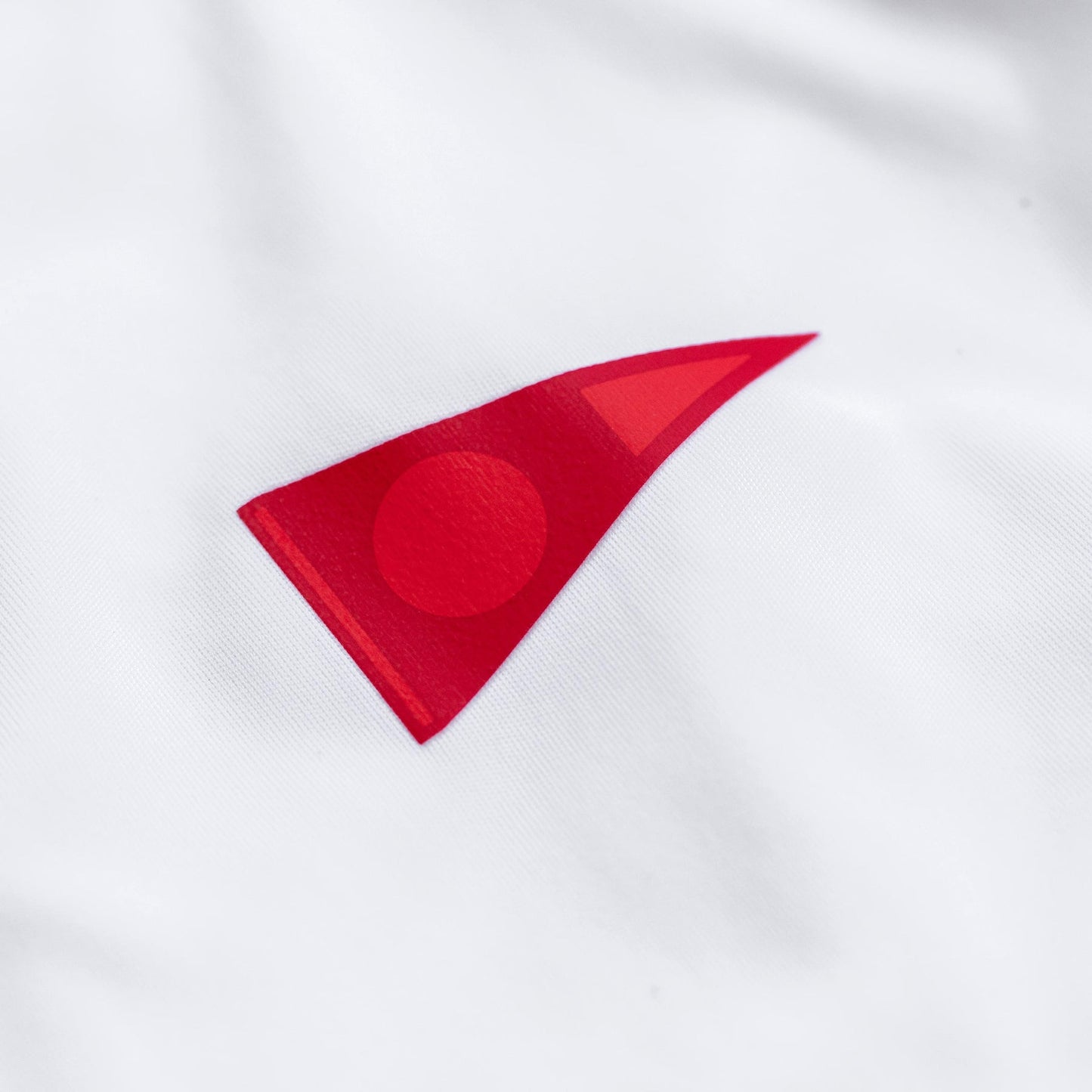 Close-up of red logo detail on white long-sleeve shirt.
