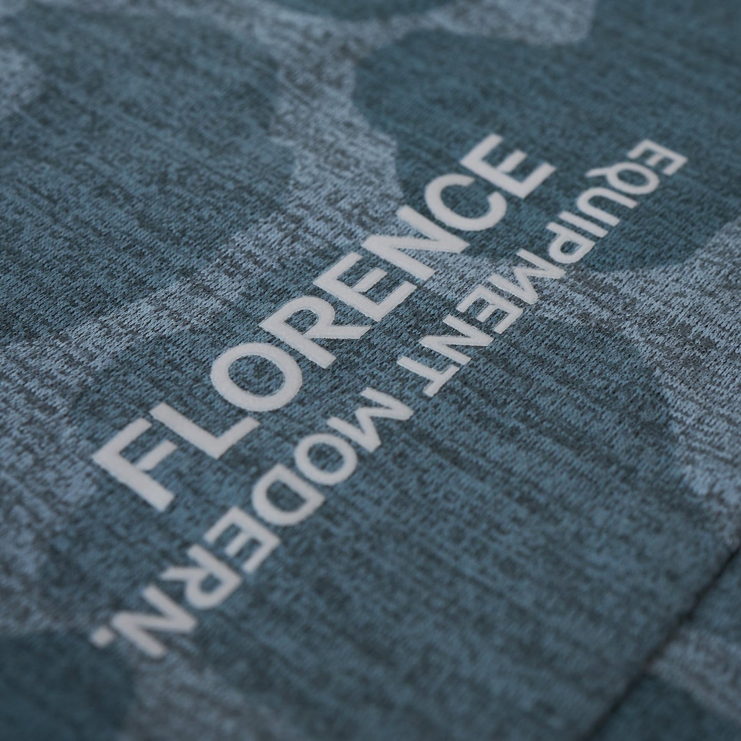 Close-up of teal long-sleeve shirt's fabric texture with white lettering.
