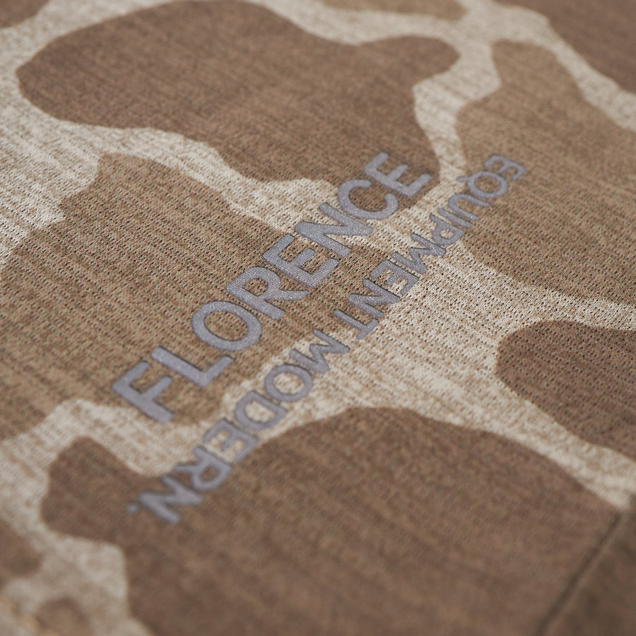 Close-up of a taupe long-sleeve shirt with a subtle camouflage pattern and embroidered text.
