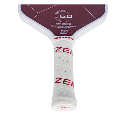 Close-up of a pickleball paddle's grip, showcasing its white perforated design and maroon accents.
