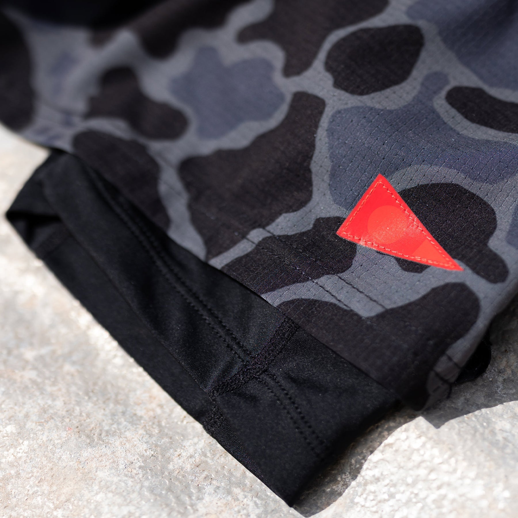 Close-up of gray camo print utility shorts with black inner lining and a red triangular detail.
