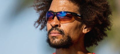 Man wearing matte black sunglasses with AC Red lenses outdoors.
