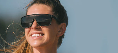 Woman smiling outdoors wearing large, dark gray sunglasses.
