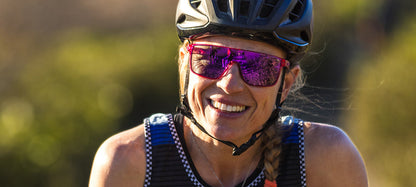 Smiling cyclist wearing purple mirrored sunglasses and helmet outdoors.
