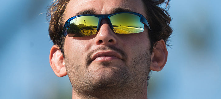 Man wearing sporty sunglasses with mirrored lenses outdoors.
