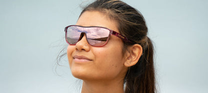 Woman wearing stylish blush pink sunglasses outdoors, reflecting a scenic view.
