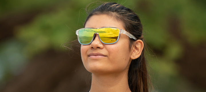 Woman outdoors wearing stylish sunglasses with mirrored lenses reflecting a scenic view.
