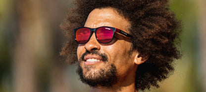 Man wearing stylish red mirror sunglasses outdoors.
