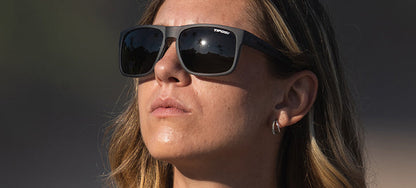 Woman wearing matte gray sunglasses outdoors, reflecting sunlight.
