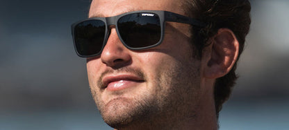 Man wearing matte black square sunglasses outdoors.
